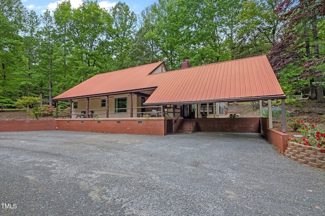 view of front facade featuring a chimney, driveway, metal roof, and a carport