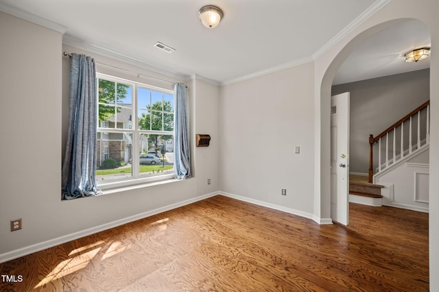 empty room featuring crown molding, arched walkways, baseboards, wood finished floors, and visible vents