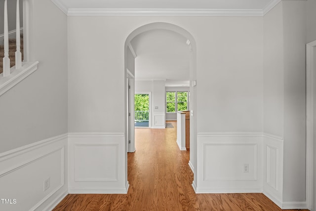 corridor featuring ornamental molding, wainscoting, wood finished floors, a decorative wall, and arched walkways
