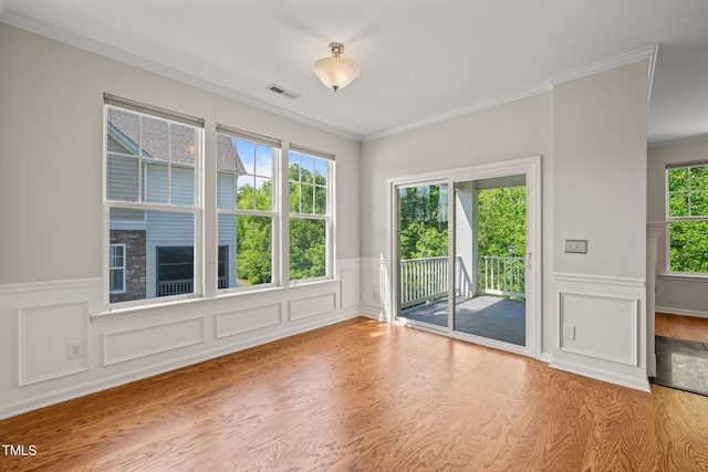 empty room featuring visible vents, ornamental molding, wood finished floors, and a wainscoted wall