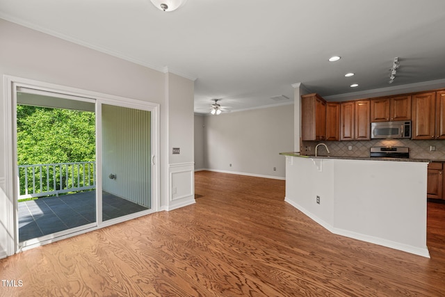 kitchen with tasteful backsplash, brown cabinets, wood finished floors, ornamental molding, and stainless steel appliances