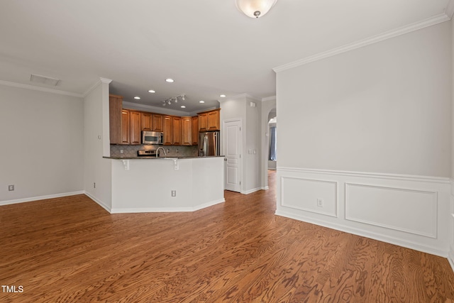 kitchen with a kitchen breakfast bar, brown cabinetry, a peninsula, ornamental molding, and stainless steel appliances