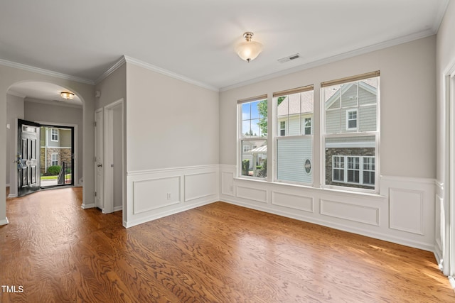 spare room featuring visible vents, crown molding, wainscoting, wood finished floors, and arched walkways
