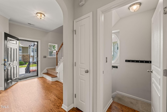entryway featuring crown molding, arched walkways, wood finished floors, baseboards, and stairs