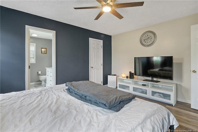 bedroom with baseboards, ensuite bathroom, a textured ceiling, and wood finished floors