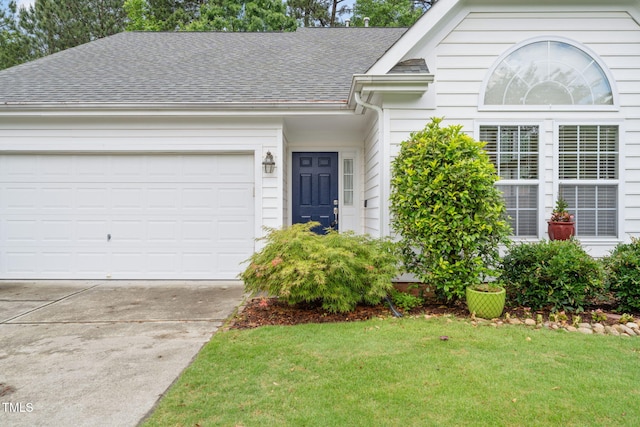 ranch-style house with concrete driveway, roof with shingles, an attached garage, and a front yard