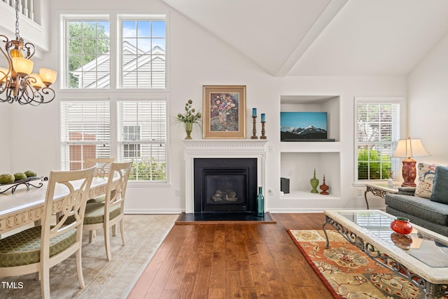 living room featuring wood-type flooring, built in features, baseboards, a glass covered fireplace, and a chandelier