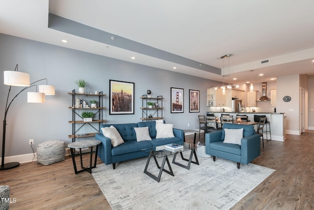 living area with recessed lighting, baseboards, wood finished floors, and a tray ceiling