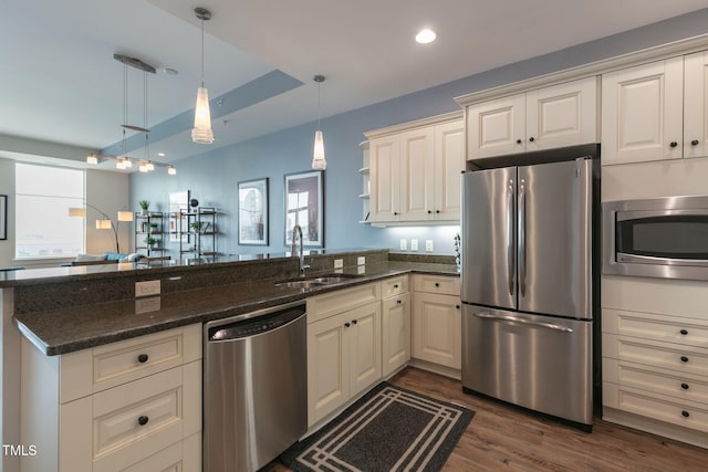 kitchen featuring a sink, dark stone countertops, a peninsula, dark wood-style floors, and stainless steel appliances