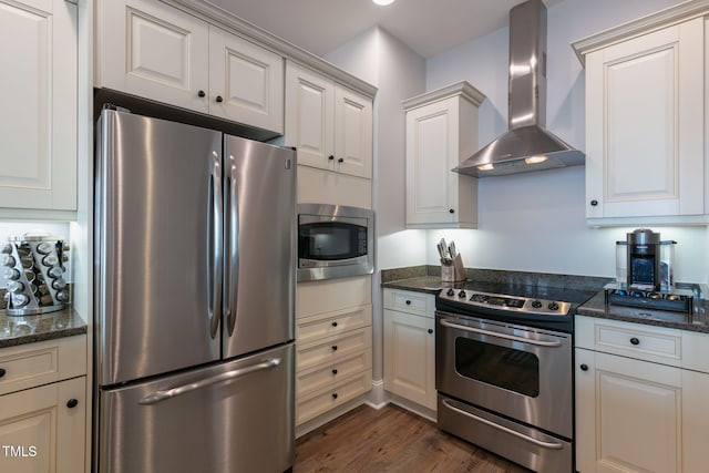 kitchen featuring dark wood-type flooring, dark stone counters, wall chimney range hood, and stainless steel appliances