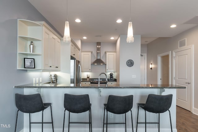 kitchen with wall chimney range hood, pendant lighting, freestanding refrigerator, a peninsula, and a breakfast bar