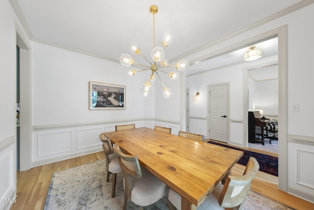 dining room with crown molding, an inviting chandelier, a decorative wall, light wood-type flooring, and a wainscoted wall