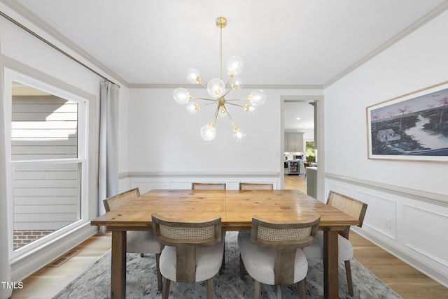 dining space featuring visible vents, ornamental molding, wainscoting, light wood-style flooring, and a notable chandelier