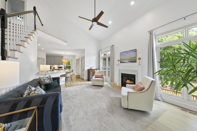 living area featuring ceiling fan, light wood-style floors, a premium fireplace, high vaulted ceiling, and visible vents