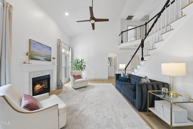 living area featuring ceiling fan, visible vents, a tiled fireplace, wood finished floors, and high vaulted ceiling