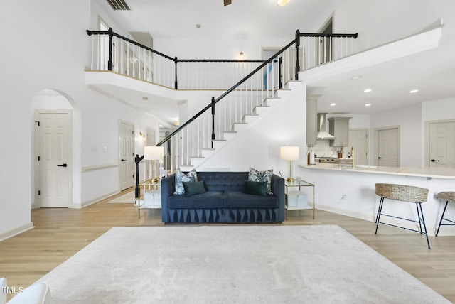 living room with stairs, a towering ceiling, wood finished floors, baseboards, and arched walkways