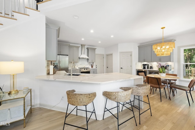 kitchen with wall chimney range hood, stainless steel appliances, gray cabinets, and a peninsula