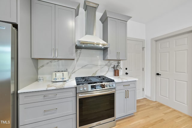 kitchen with appliances with stainless steel finishes, gray cabinets, light wood-style flooring, and wall chimney exhaust hood