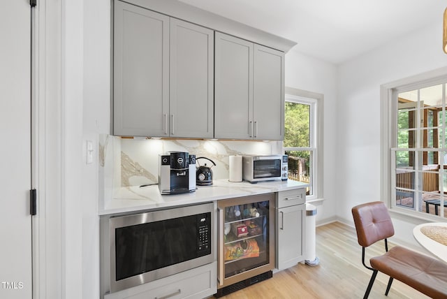 bar featuring built in microwave, a toaster, baseboards, light wood finished floors, and beverage cooler