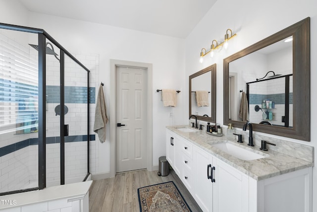 full bath with a sink, double vanity, a stall shower, and wood finished floors