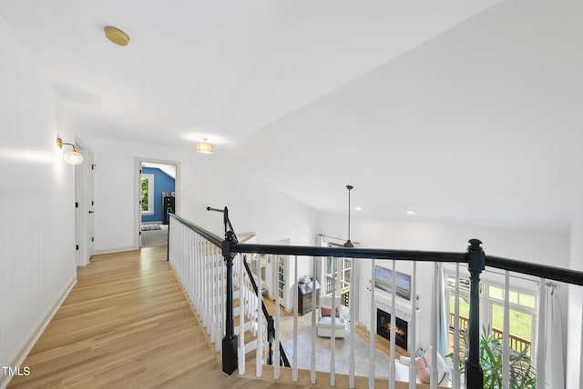 hallway with baseboards, an upstairs landing, vaulted ceiling, and light wood-type flooring