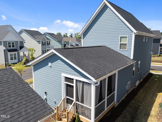 rear view of house featuring a sunroom, roof with shingles, and a residential view