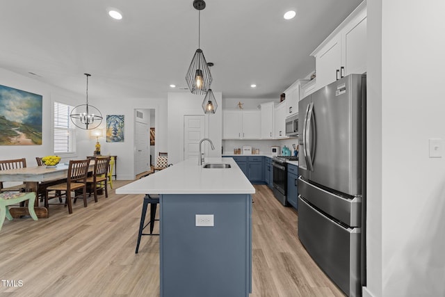 kitchen featuring a kitchen breakfast bar, appliances with stainless steel finishes, a sink, light countertops, and light wood-style floors