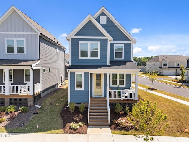 traditional-style house featuring a front lawn, covered porch, stairs, a shingled roof, and board and batten siding