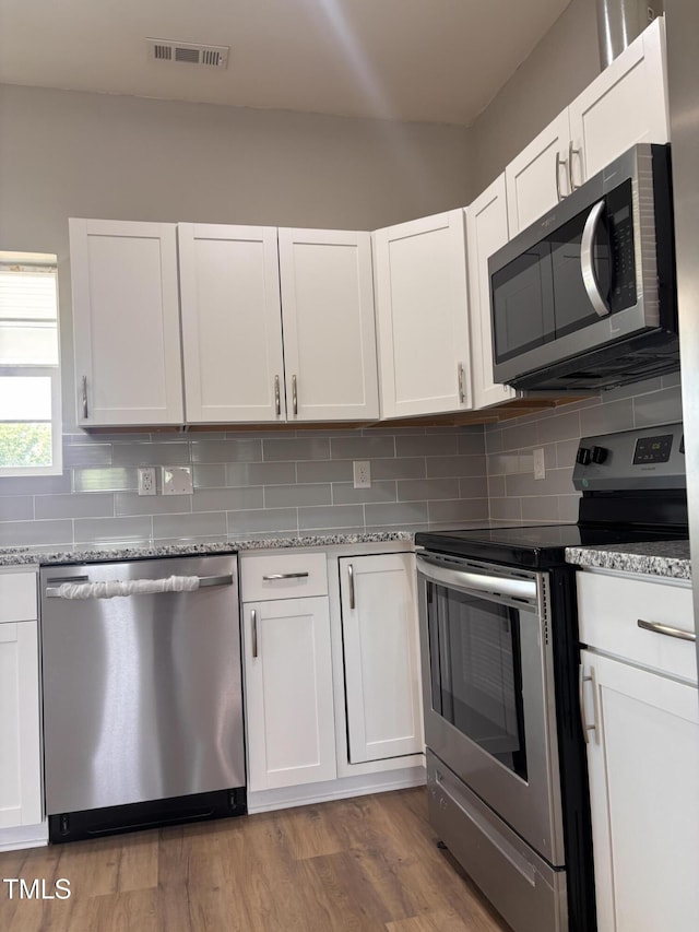5029 Carole Dr, Wilson, NC 27893 - kitchen with appliances with stainless steel finishes, backsplash, light wood-style floors, light stone counters, and white cabinets
