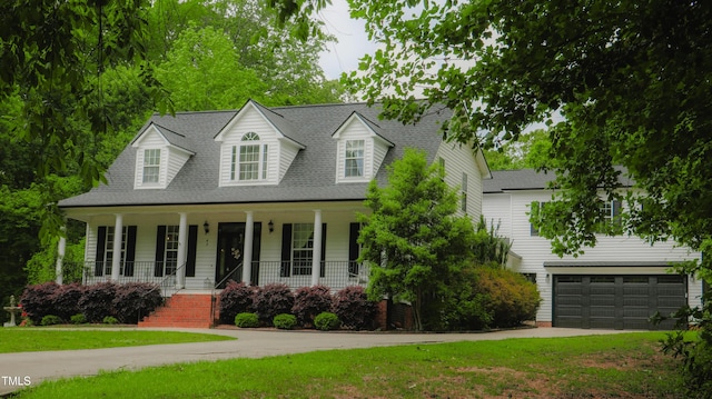 cape cod-style house featuring an attached garage, a front yard, a shingled roof, concrete driveway, and a porch