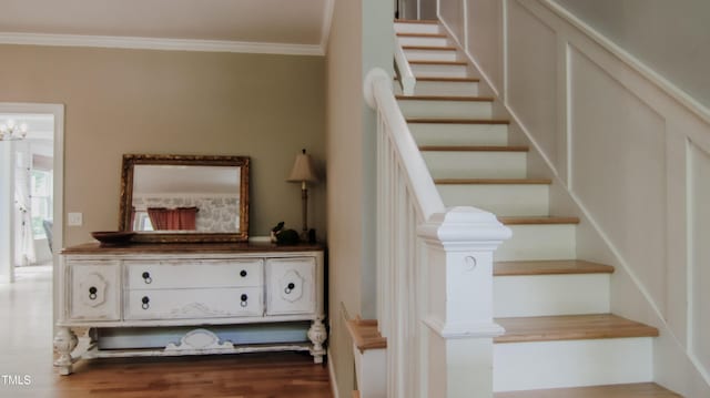 stairway with ornamental molding and wood finished floors
