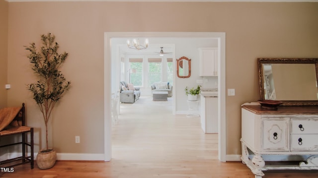 corridor featuring light wood-style floors, baseboards, and an inviting chandelier