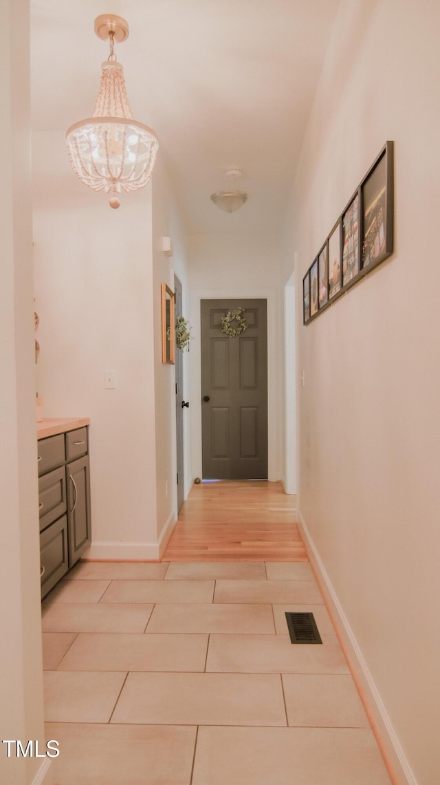 hallway with light tile patterned floors, baseboards, visible vents, and an inviting chandelier
