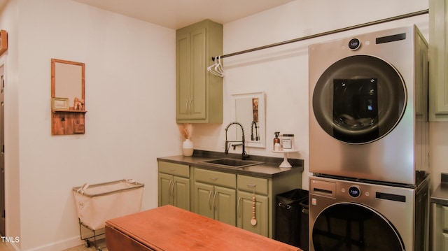 washroom featuring cabinet space, baseboards, stacked washing maching and dryer, and a sink