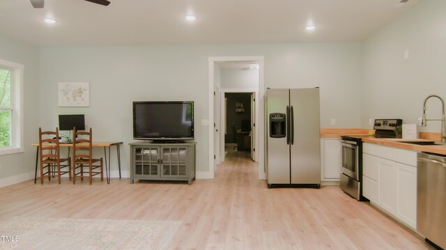 kitchen with a sink, white cabinets, stainless steel appliances, and light wood-style flooring