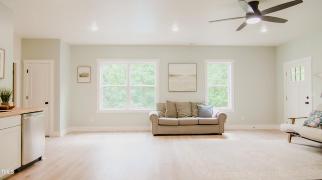 living area with baseboards, ceiling fan, a wealth of natural light, and light wood-style floors