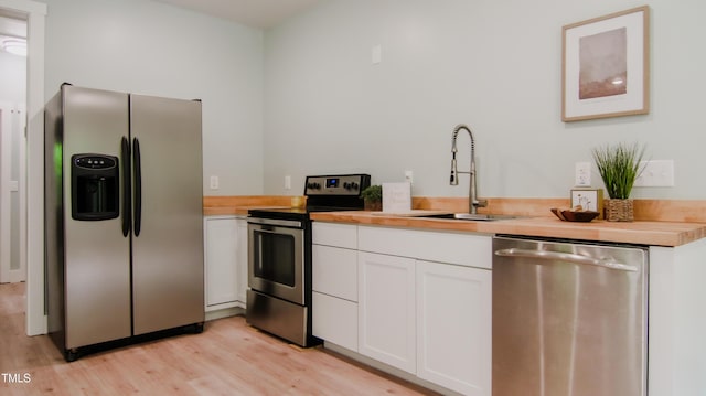 kitchen with butcher block countertops, white cabinets, a sink, light wood finished floors, and appliances with stainless steel finishes