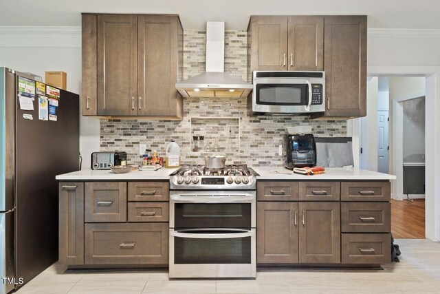 kitchen with crown molding, wall chimney range hood, light countertops, backsplash, and stainless steel appliances