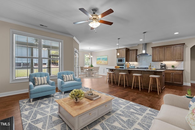 living area featuring crown molding, dark wood-style flooring, ceiling fan with notable chandelier, baseboards, and visible vents