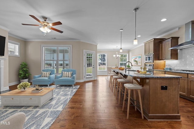 kitchen featuring wall chimney range hood, a breakfast bar area, stainless steel appliances, and dark wood-style floors