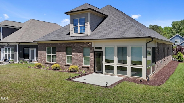 rear view of property featuring a lawn, a shingled roof, a patio area, and brick siding