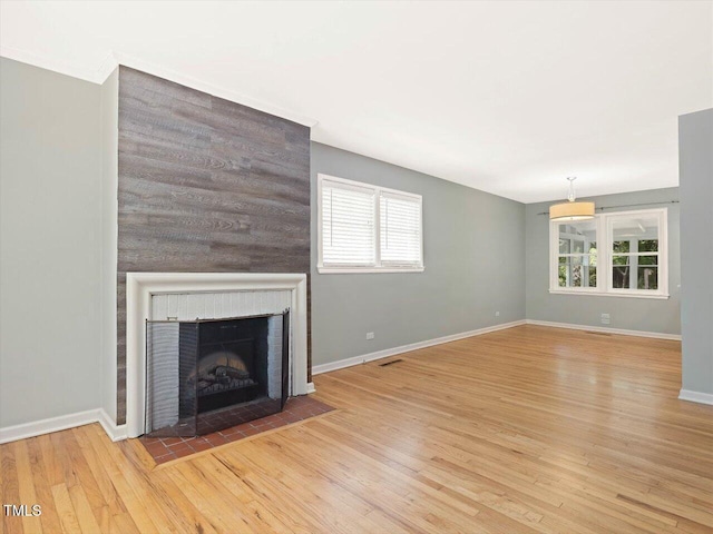 unfurnished living room featuring plenty of natural light, wood finished floors, baseboards, and a brick fireplace