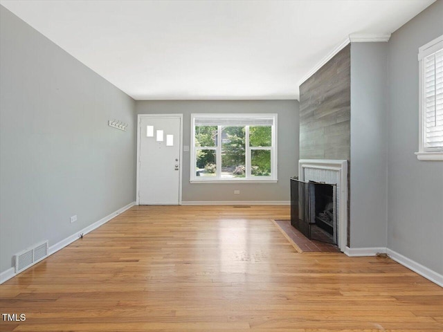 unfurnished living room with a large fireplace, light wood-type flooring, visible vents, and baseboards