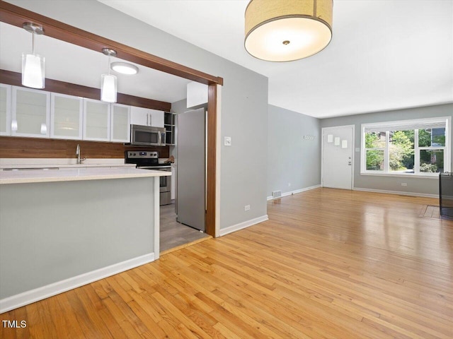 kitchen with stainless steel appliances, decorative light fixtures, white cabinetry, light countertops, and light wood-style floors