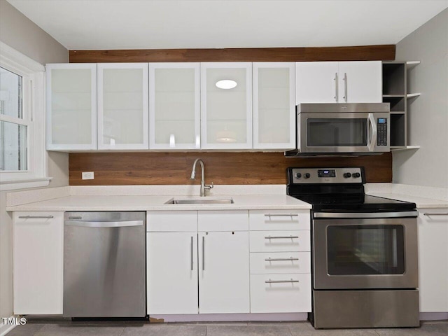kitchen with a sink, white cabinetry, light countertops, glass insert cabinets, and appliances with stainless steel finishes