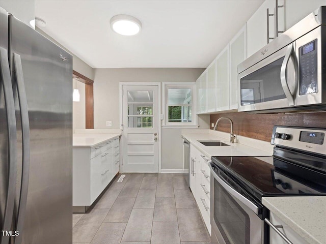 kitchen with light tile patterned floors, a sink, stainless steel appliances, white cabinetry, and baseboards