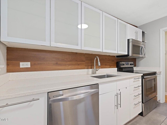 kitchen featuring light tile patterned floors, glass insert cabinets, a sink, white cabinetry, and appliances with stainless steel finishes