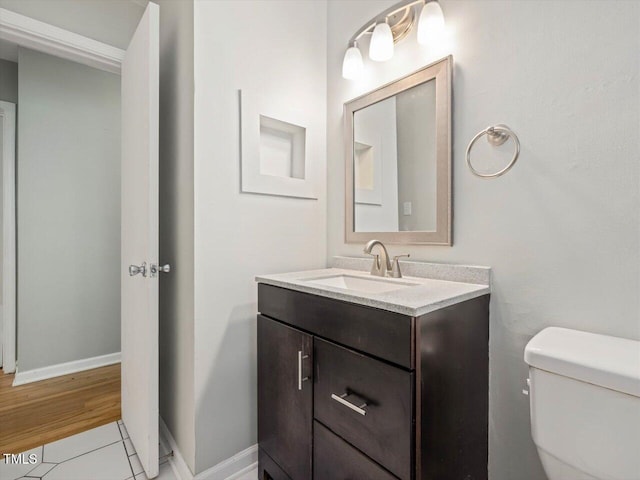 half bathroom featuring tile patterned floors, toilet, baseboards, and vanity