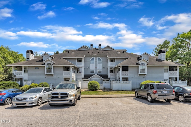 multi unit property with uncovered parking, roof with shingles, fence, and a chimney