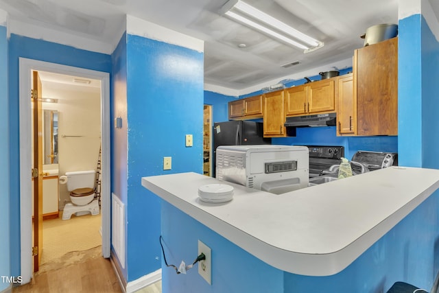 kitchen with a peninsula, light wood-type flooring, visible vents, under cabinet range hood, and electric stove